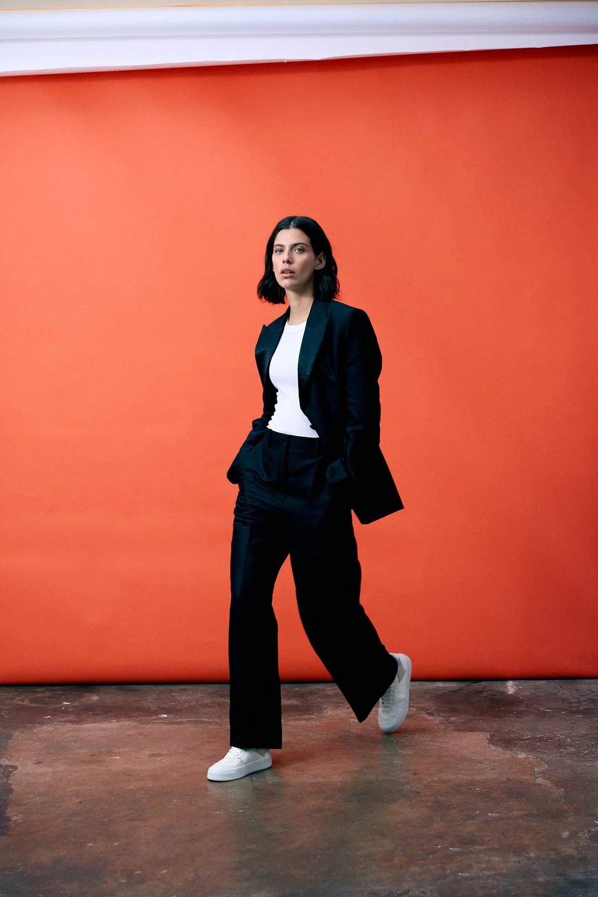 Copenhagen Studios, Model im schwarzen Anzug und weißen Sneakern läuft vor knallorangem Hintergrund, Kampagne Oktober 2022, fotografiert von Kilian Amrehn