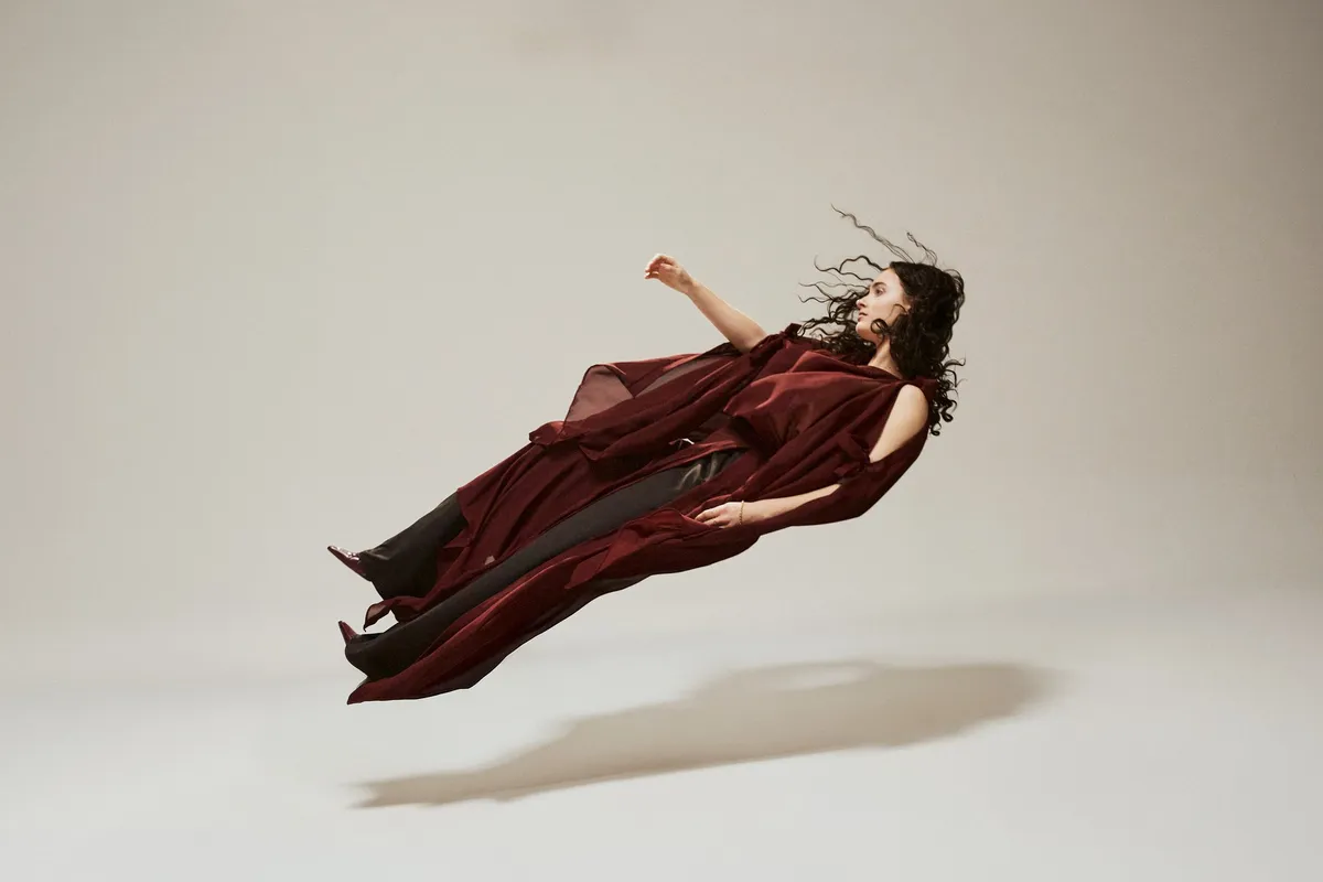 Ozean der Stille, Model mit Locken scheint im weinroten Chiffon-Outfit rückwärts über dem Boden zu schweben, helles Studio, Modestrecke 2026, fotografiert von Kilian Amrehn