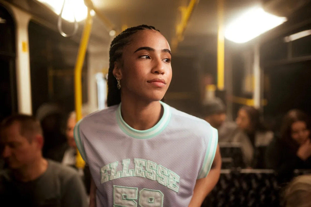Peek & Cloppenburg x Ellesse, Model mit geflochtenen Zöpfen im hellen Ellesse-Mesh-Shirt in einer nächtlichen Straßenbahn, warmes Licht, Kampagne 2022, fotografiert von Kilian Amrehn