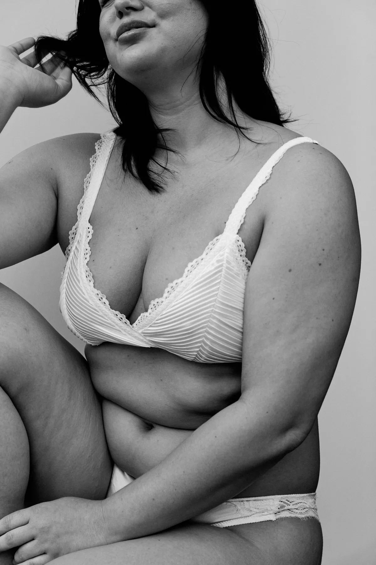 Phiala, Model mit dunklem Haar in weißem Plissee-BH mit Spitze, natürliche Kurven, entspannte Pose in Schwarzweiß, Kampagne 2024, fotografiert von Kilian Amrehn