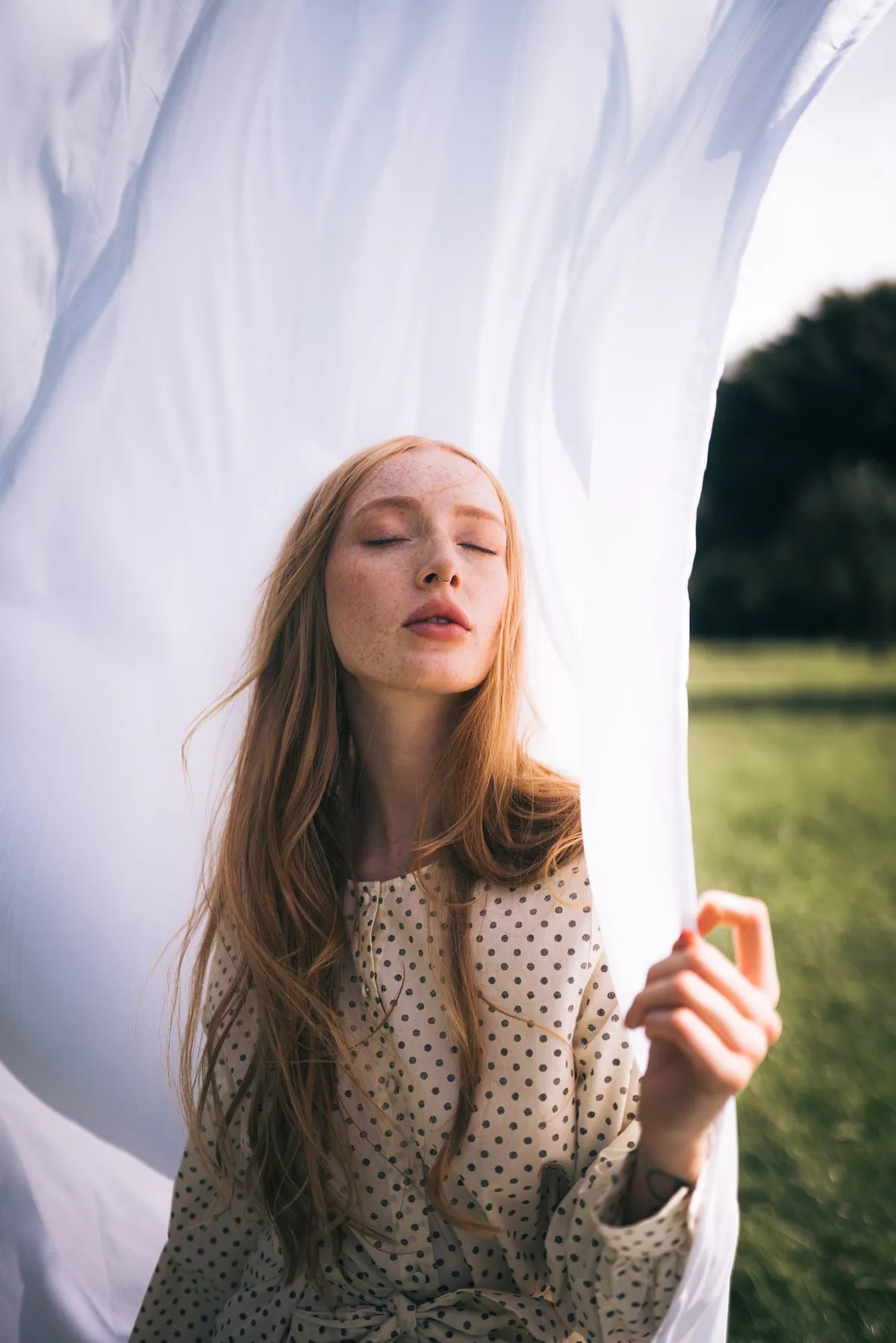 Rock Fairyland, rothaariges Model mit Sommersprossen und gepunktetem Kleid vor wehendem weißem Tuch auf einer Wiese, Editorial 2021, fotografiert von Kilian Amrehn