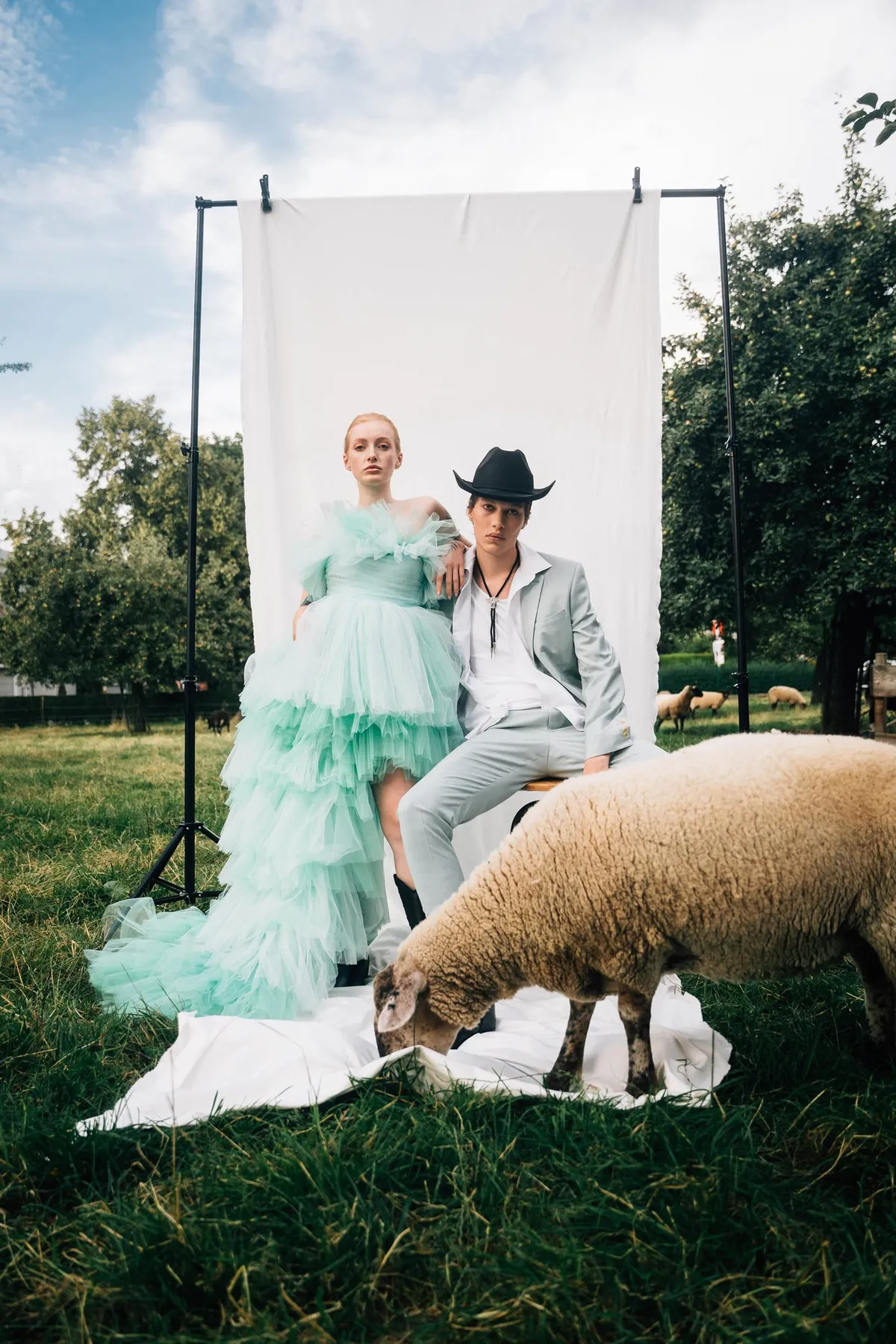 Rock Fairyland, Model im mintgrünen Tüllkleid und Model mit Cowboyhut vor weißem Hintergrundtuch auf einer Schafweide, Editorial 2021, fotografiert von Kilian Amrehn