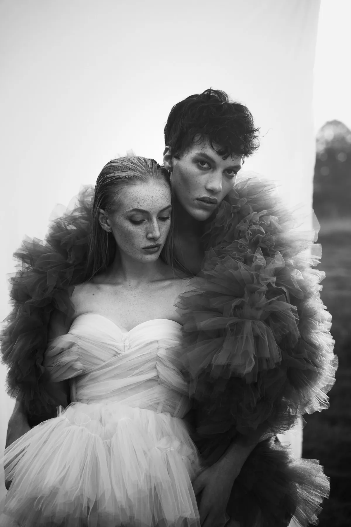 Rock Fairyland, Model mit dunklen Locken umarmt Model im weißen Tüllkleid von hinten, voluminöser Tüll in Schwarzweiß, Editorial 2021, fotografiert von Kilian Amrehn
