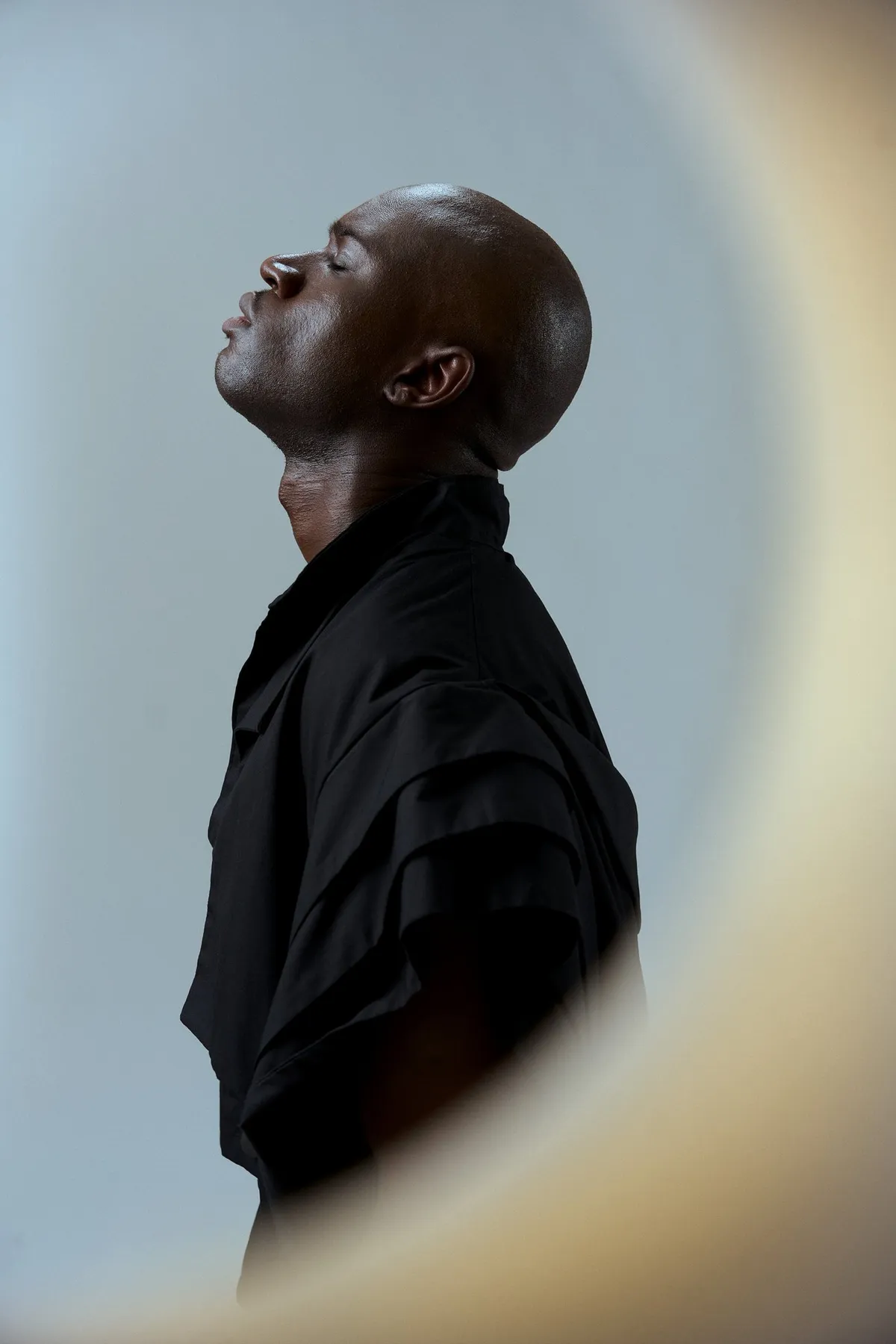 JEREMIAH Silent Escape, Model im schwarzen Hemd im Profil mit geschlossenen Augen, durch eine runde Öffnung fotografiert, Kampagne 2024, fotografiert von Kilian Amrehn