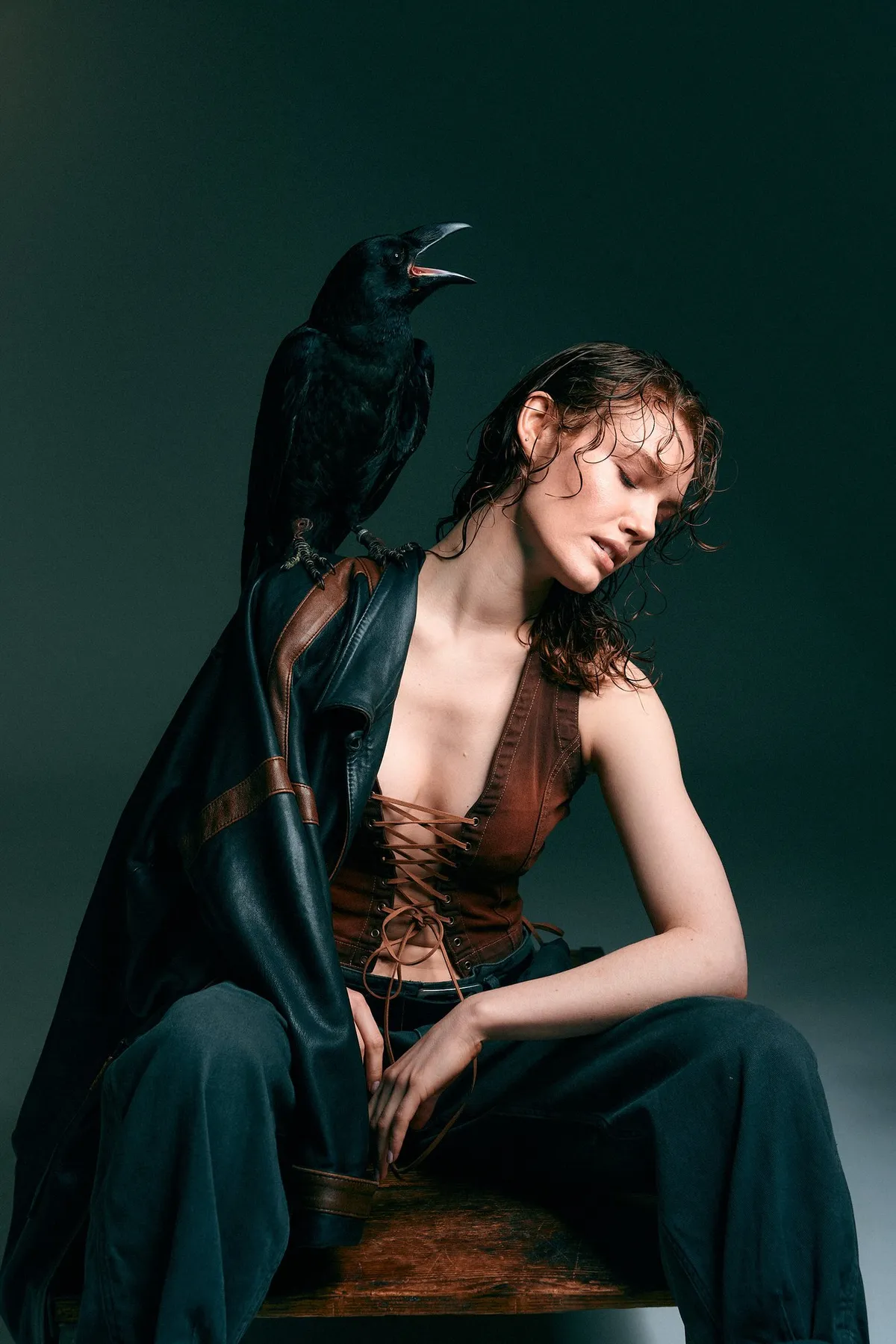 Untamed, Model mit nassem Haar in Lederweste mit Schnürung und offenem Mantel, ein Rabe auf der Schulter, dunkelgrüner Grund, Editorial 2024, fotografiert von Kilian Amrehn